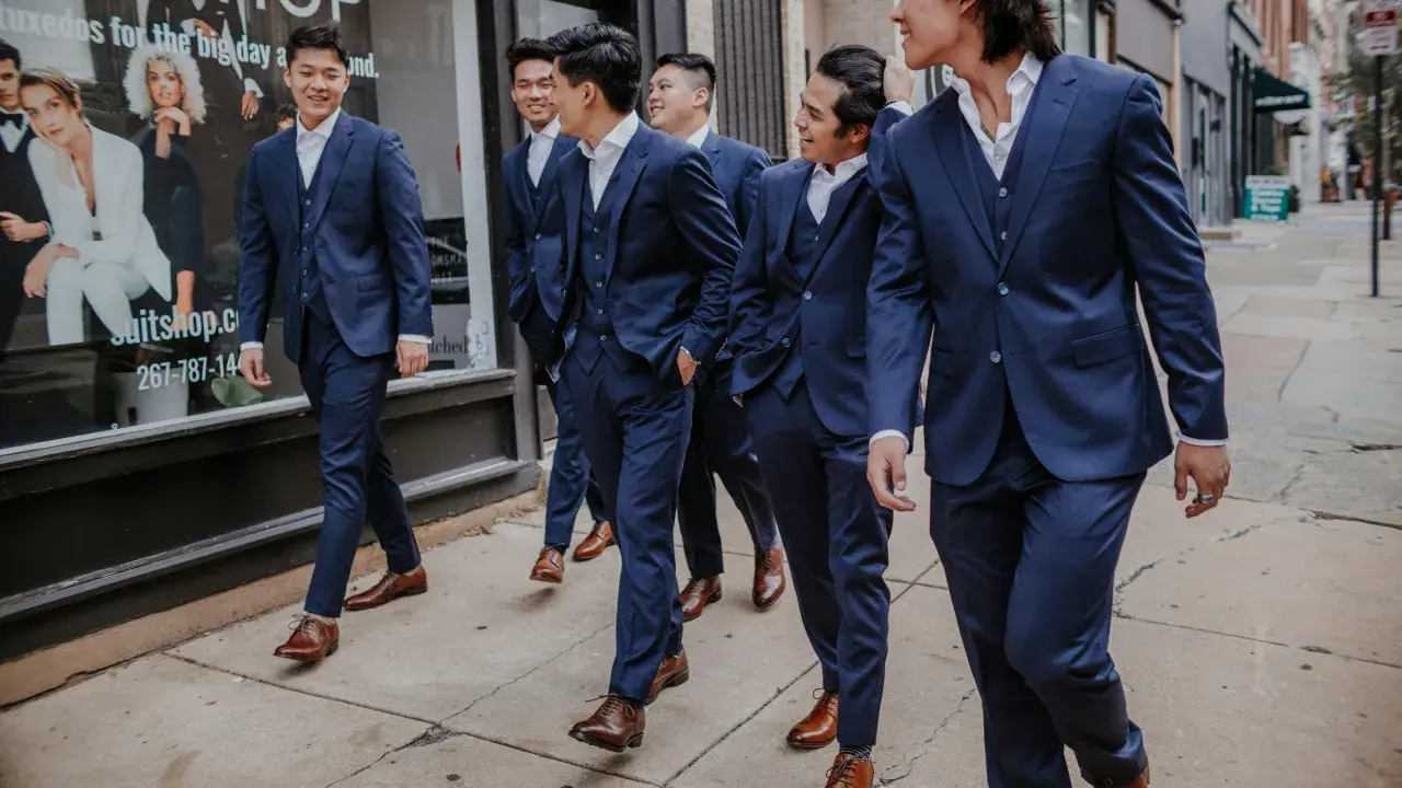 A group of men in navy suits walk down a sidewalk. They are all wearing brown dress shoes, proving you can wear brown shoes with a navy suit.