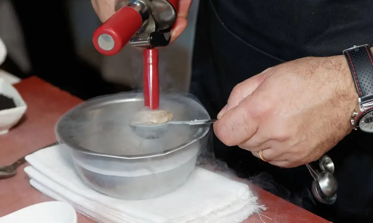 Chef usa sifón para crear texturas aireadas, ideal para recetas de espumas para sifón. Humo frío rodea el bol.