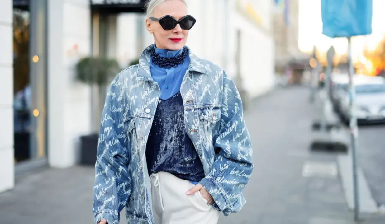 Kobieta w oversize'owej jeansowej katanie z nadrukiem, niebieskiej koszuli i błyszczącym topie.