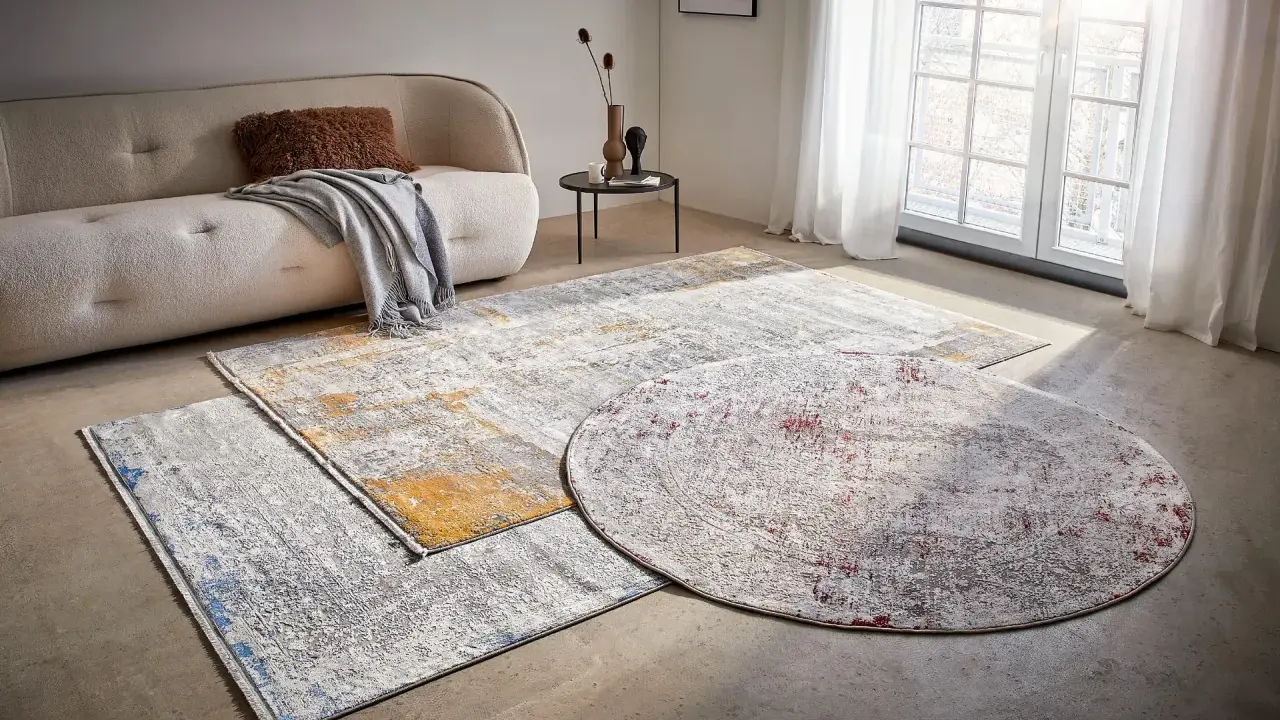 Mattor inspiration: En rund och två rektangulära mattor med abstrakt mönster i grått, vitt, gult och rött ligger på ett betonggolv framför en soffa.