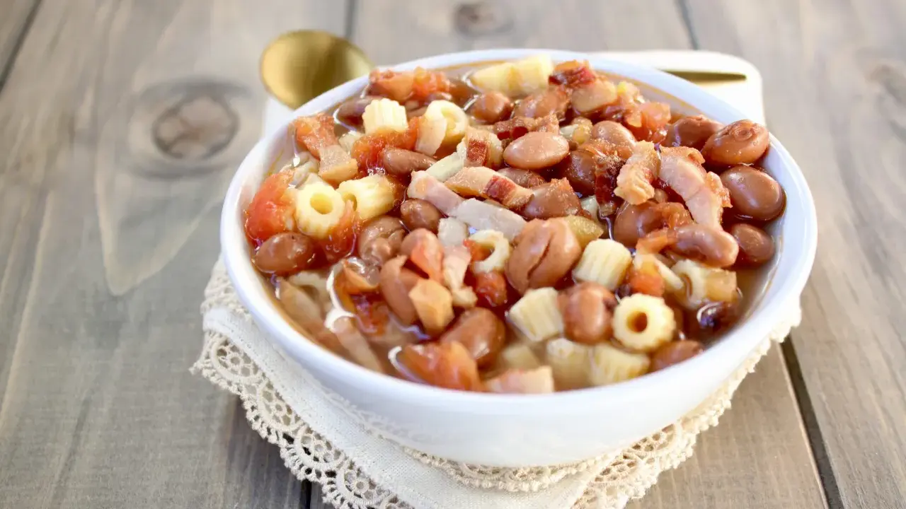 Una ciotola di pasta e fagioli in scatola, con pomodoro e pancetta, servita su un tovagliolo di pizzo.