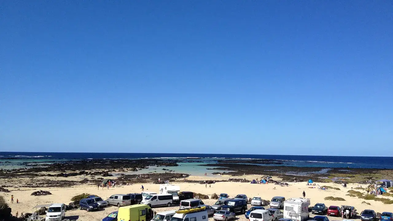 Día soleado en Lanzarote con niños. Coches aparcados en la playa, familias disfrutando del mar y la arena.