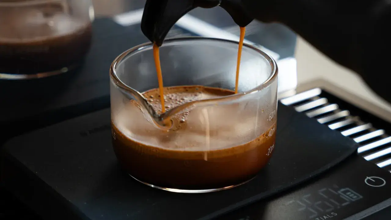 Frisch gebrühter Espresso fließt in ein Glasgefäß, die goldbraune crema de cafe bildet eine samtige Schicht.