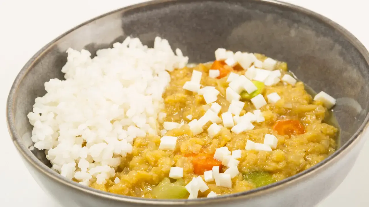Un tazón de arroz blanco junto a un guiso cremoso de lentejas rojas con trozos de queso y verduras.