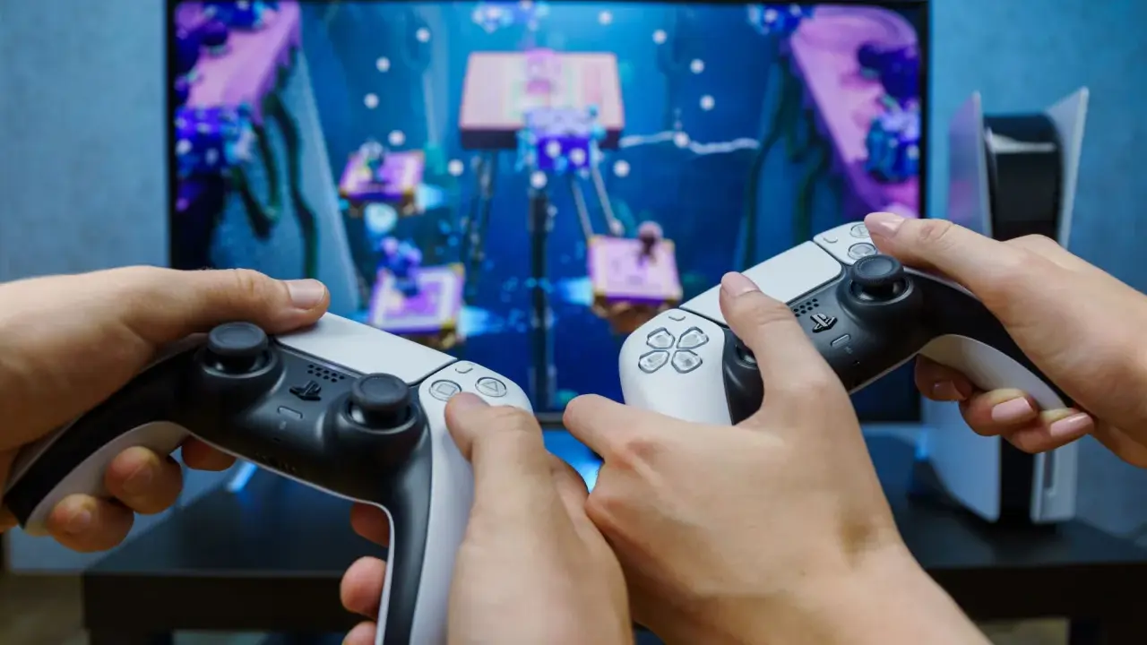 Dwie osoby grają w grę na konsoli PlayStation 5, trzymając kontrolery DualSense.