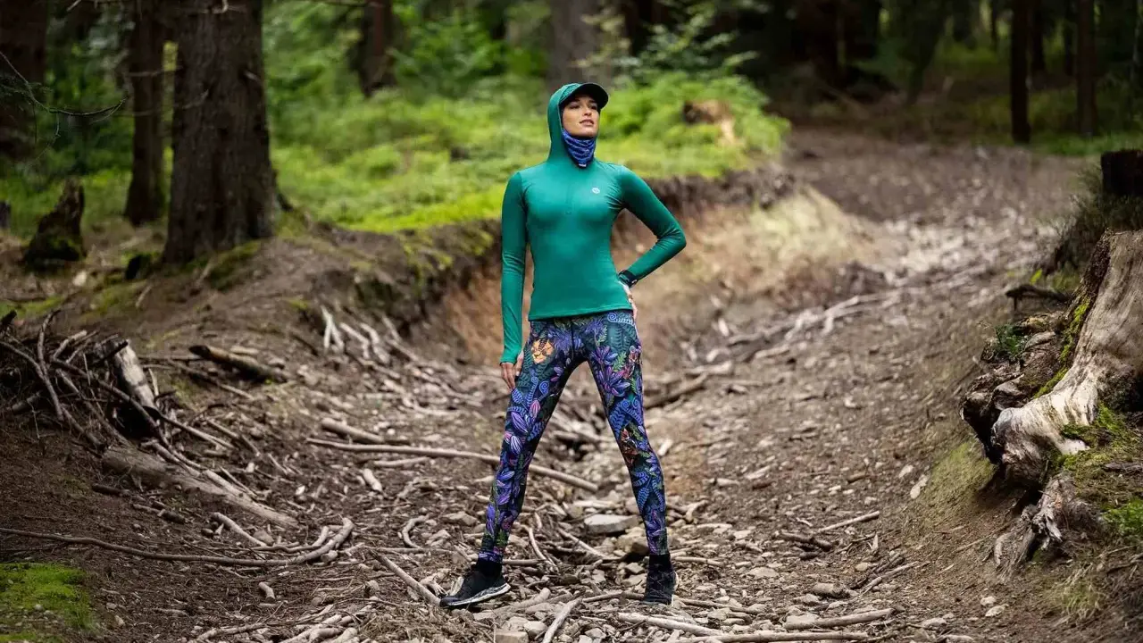 Kobieta w lesie, w kolorowych legginsach i zielonej bluzie, pokazuje, co daje stretching: elastyczność i siłę do pokonywania górskich ścieżek.
