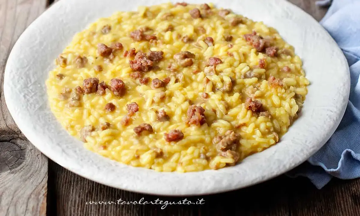 Un cremoso risotto con salsiccia, servito in un piatto bianco su un tavolo di legno rustico.