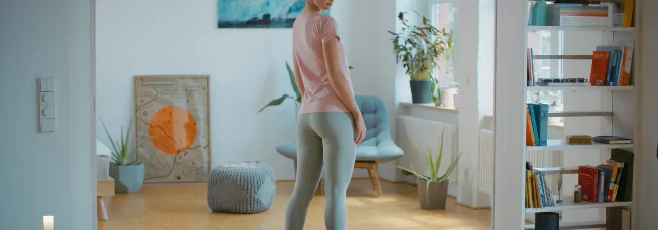 Frau in Sportkleidung, bereit für ein Workout. BWS mobilisieren für mehr Flexibilität. Bücherregal und Pflanzen im Hintergrund.