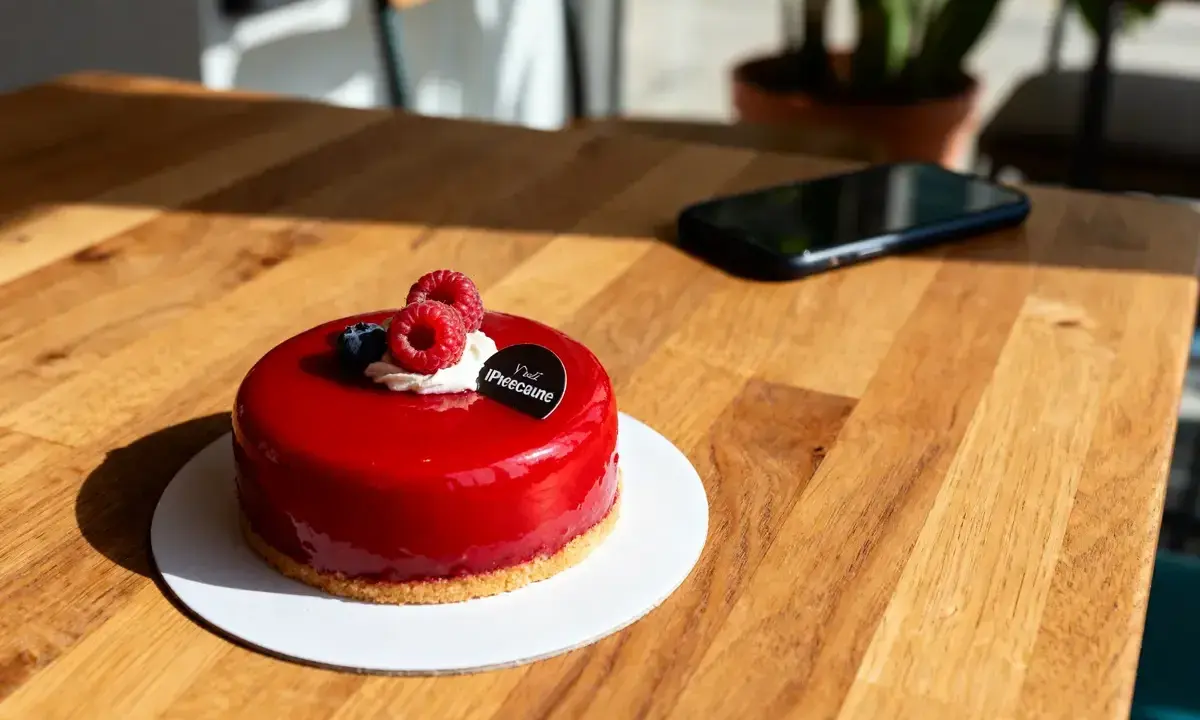 Un délicieux entremet fruit rouge, glacé et garni de framboises fraîches, attend sur une table en bois.