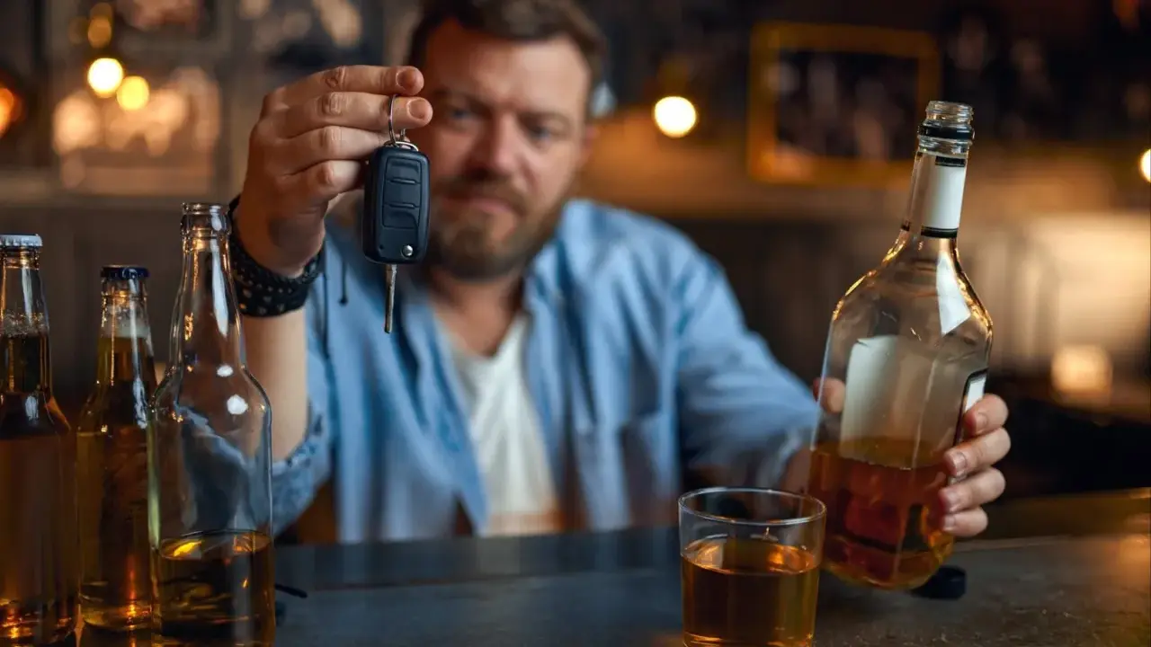 Mężczyzna trzyma kluczyki do samochodu, zastanawiając się, czy jestem pijany. Obok butelki i szklanka alkoholu.
