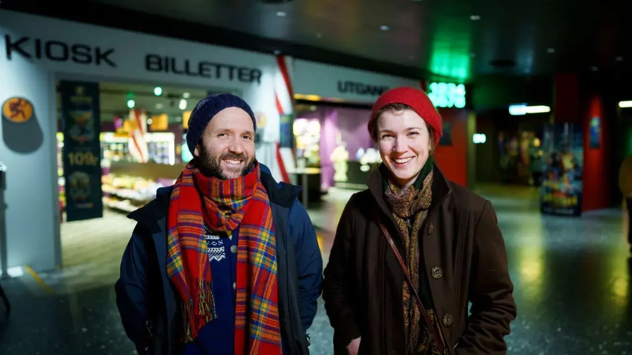 Två glada personer vid en biljettkiosk, redo att se filmer på bio nu.