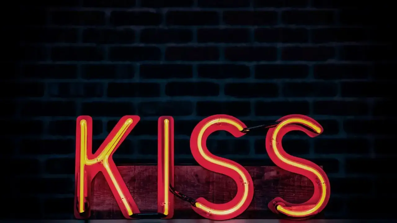 Neonowy napis KISS na tle ceglanej ściany. Zasada KISS: Keep It Simple, Stupid.