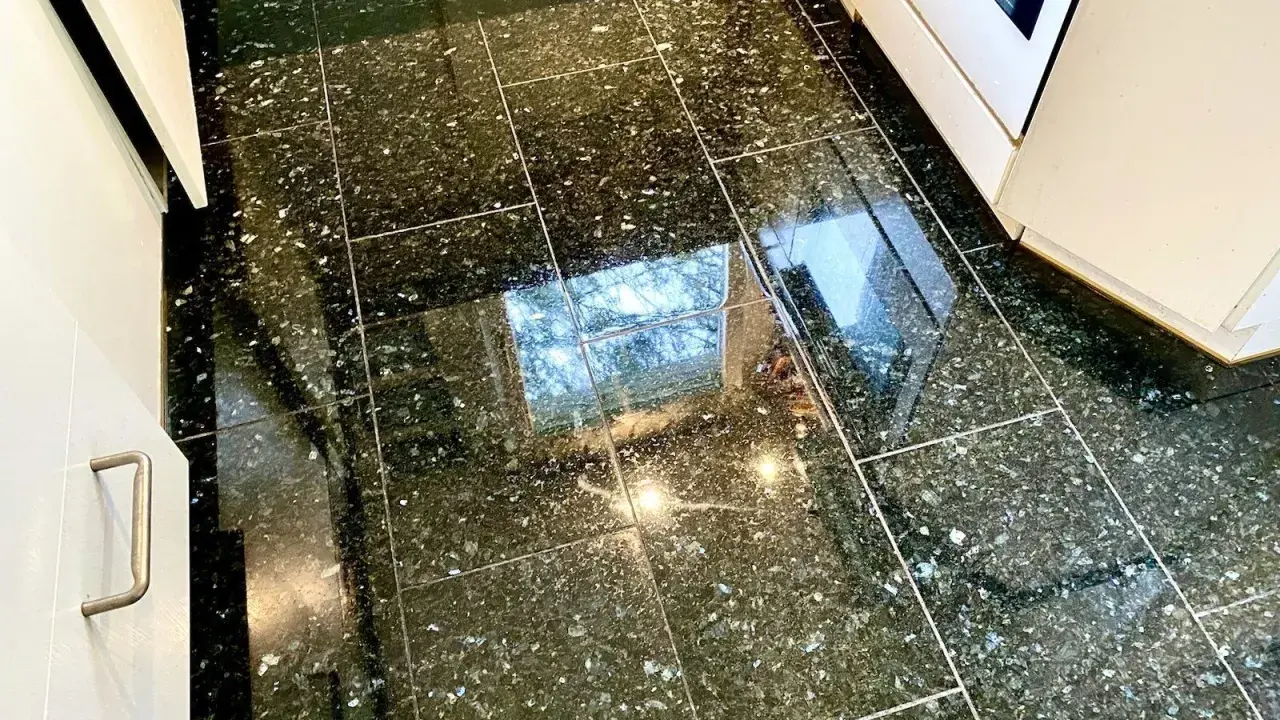 Glänzender Granitboden, der nach dem Granit reinigen strahlt. Spiegelungen von Fenstern und Lichtern auf den dunklen Fliesen.