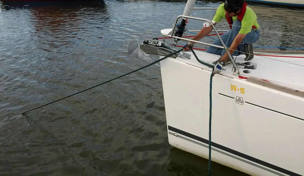 Un homme en gilet de sauvetage ajuste la pendille du bateau, une corde verte s'étendant sur l'eau calme.