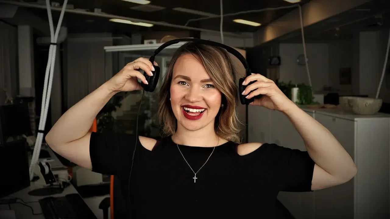 Uśmiechnięta kobieta z słuchawkami na uszach, słucha podcastów do nauki angielskiego.