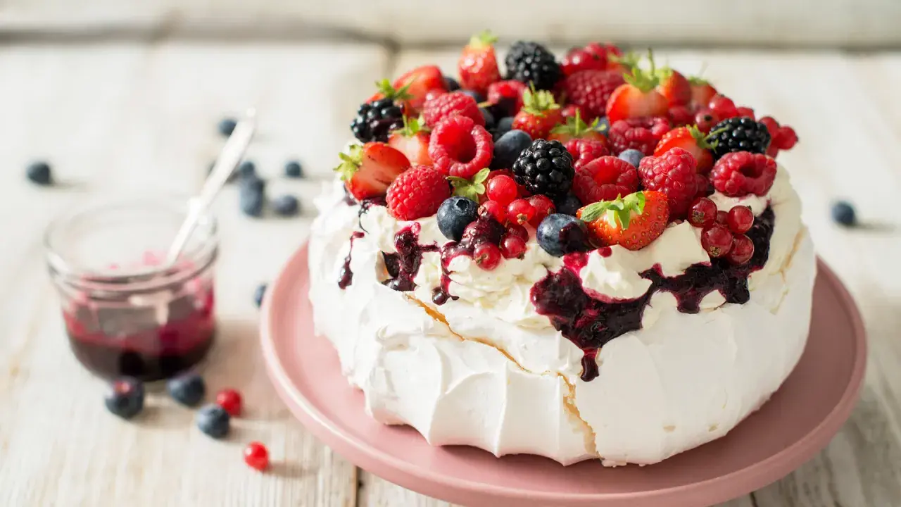 Beza pavlova która zawsze wychodzi, udekorowana bitą śmietaną i mnóstwem świeżych owoców leśnych.