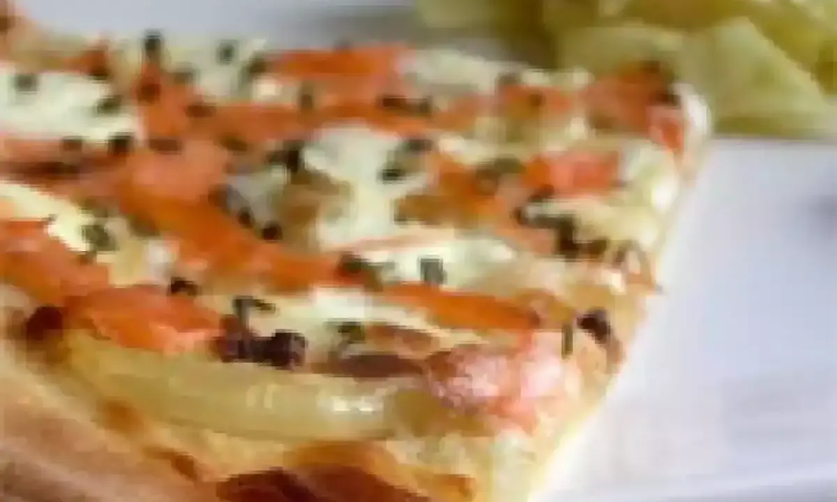 Tranche de flammekueche saumon, oignons et fromage, avec une salade verte en arrière-plan.