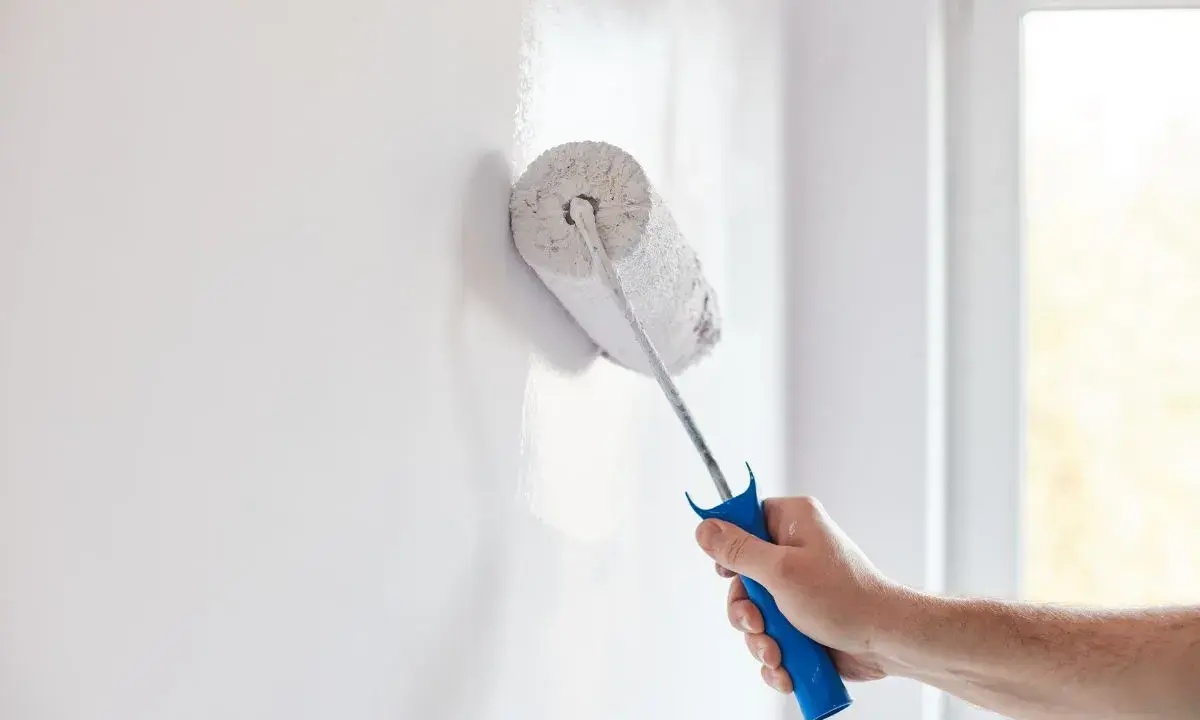Mano con rodillo pintando una pared blanca, renovando el hogar.