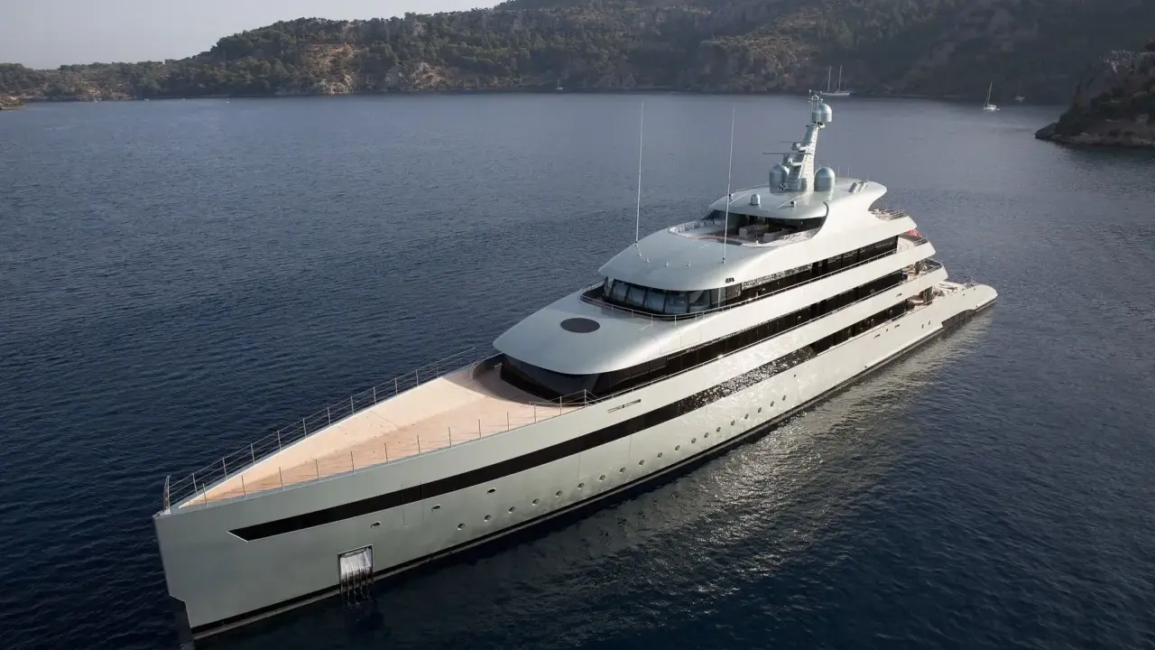 Un yacht de luxe gris clair navigue dans une baie. Le choix couleur coque bateau est élégant, contrastant avec le bleu profond de l'eau.