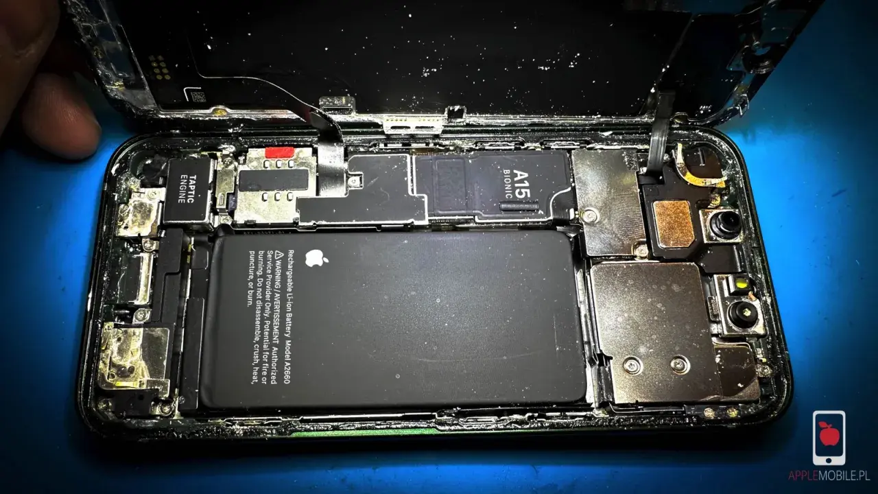 Rozkręcony iPhone z widoczną baterią i procesorem A15 Bionic. Wygląda na to, że ten zalany iPhone wymaga pilnej naprawy.