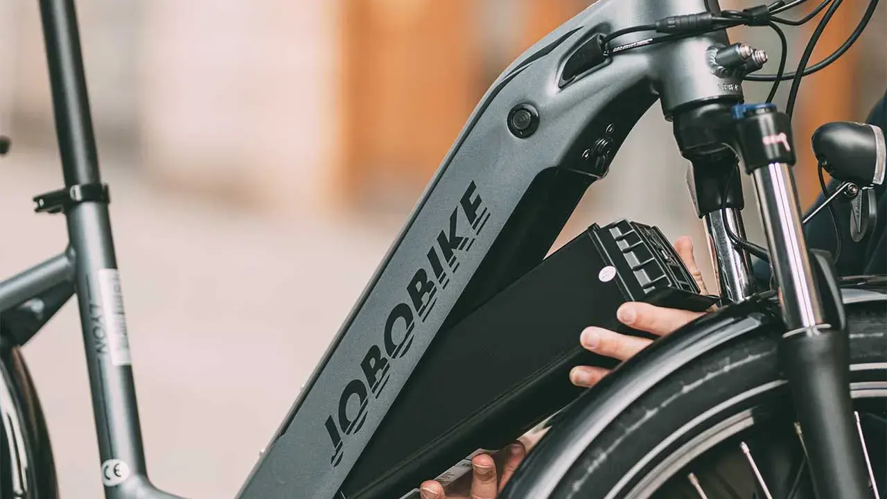 Ręce wyjmujące czarną baterię z ramy roweru elektrycznego JOBORBIKE.