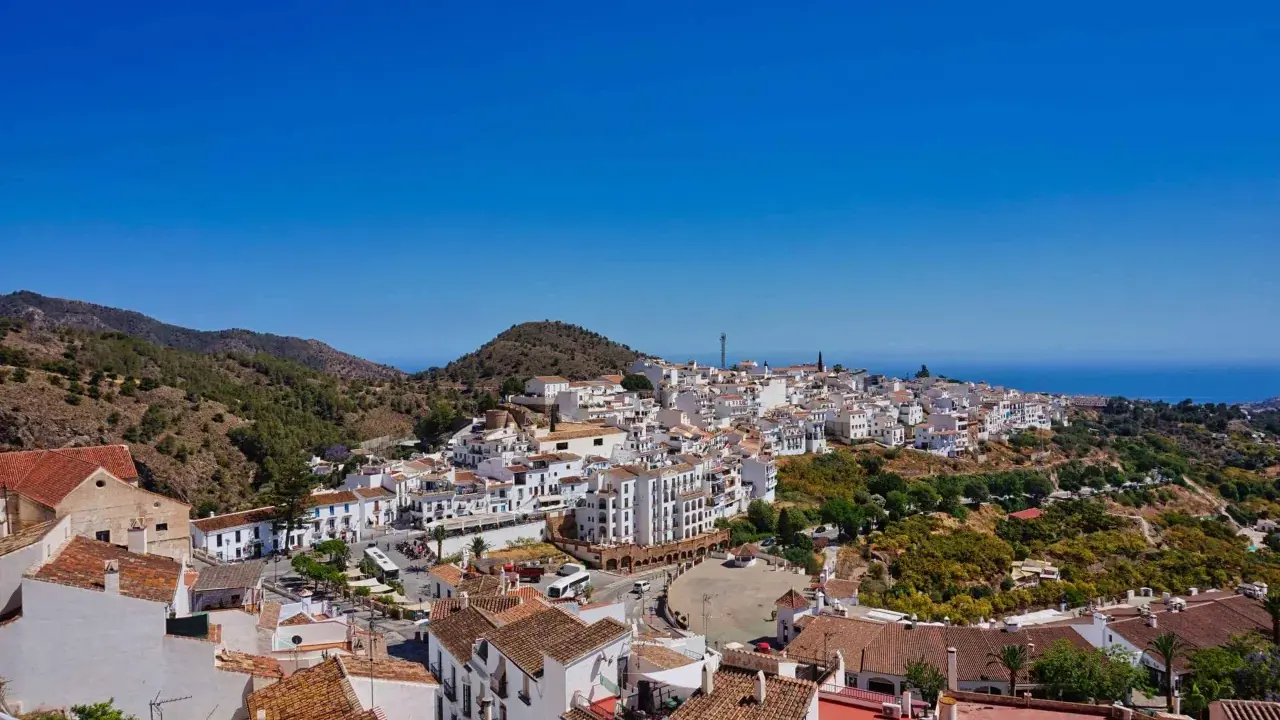 Weiß getünchte Häuser schmiegen sich an einen Hügel in Frigiliana, Spanien. Der Blick reicht über die Dächer bis zum blauen Meer.