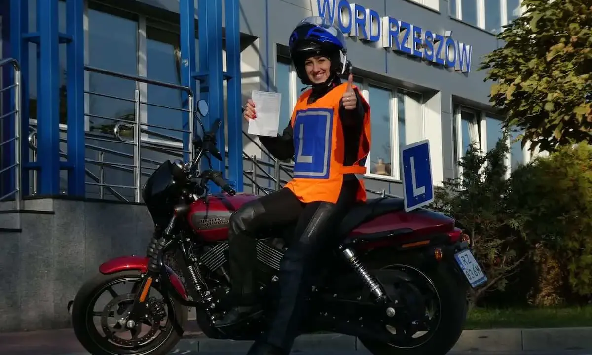Uśmiechnięta motocyklistka z dokumentem w ręku i kciukiem w górze, gotowa na egzamin teoretyczny kat A.