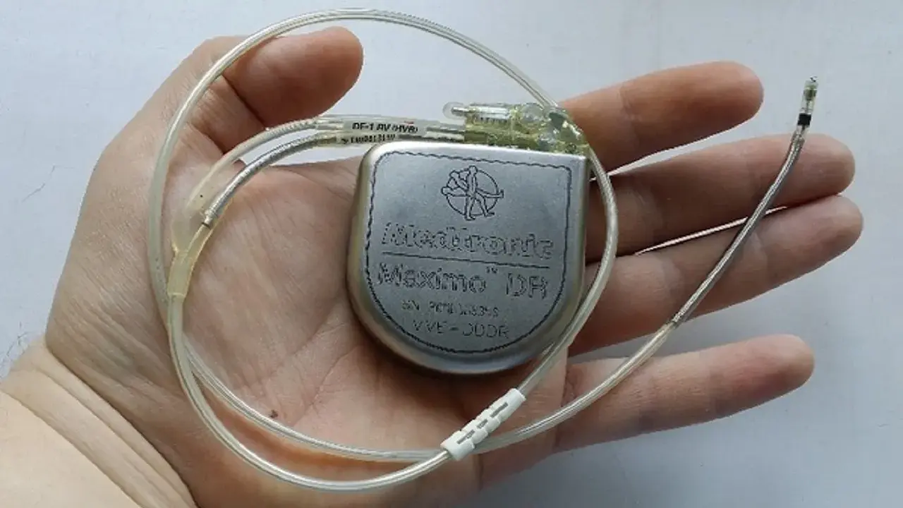 Dłoń trzyma kardiowerter Medtronic Maximo DR, urządzenie podobne do rozrusznika serca, z dwoma elektrodami.