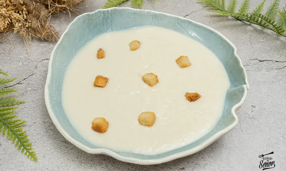 Crema de coliflor suave y cremosa, decorada con crujientes picatostes dorados en un cuenco azul.
