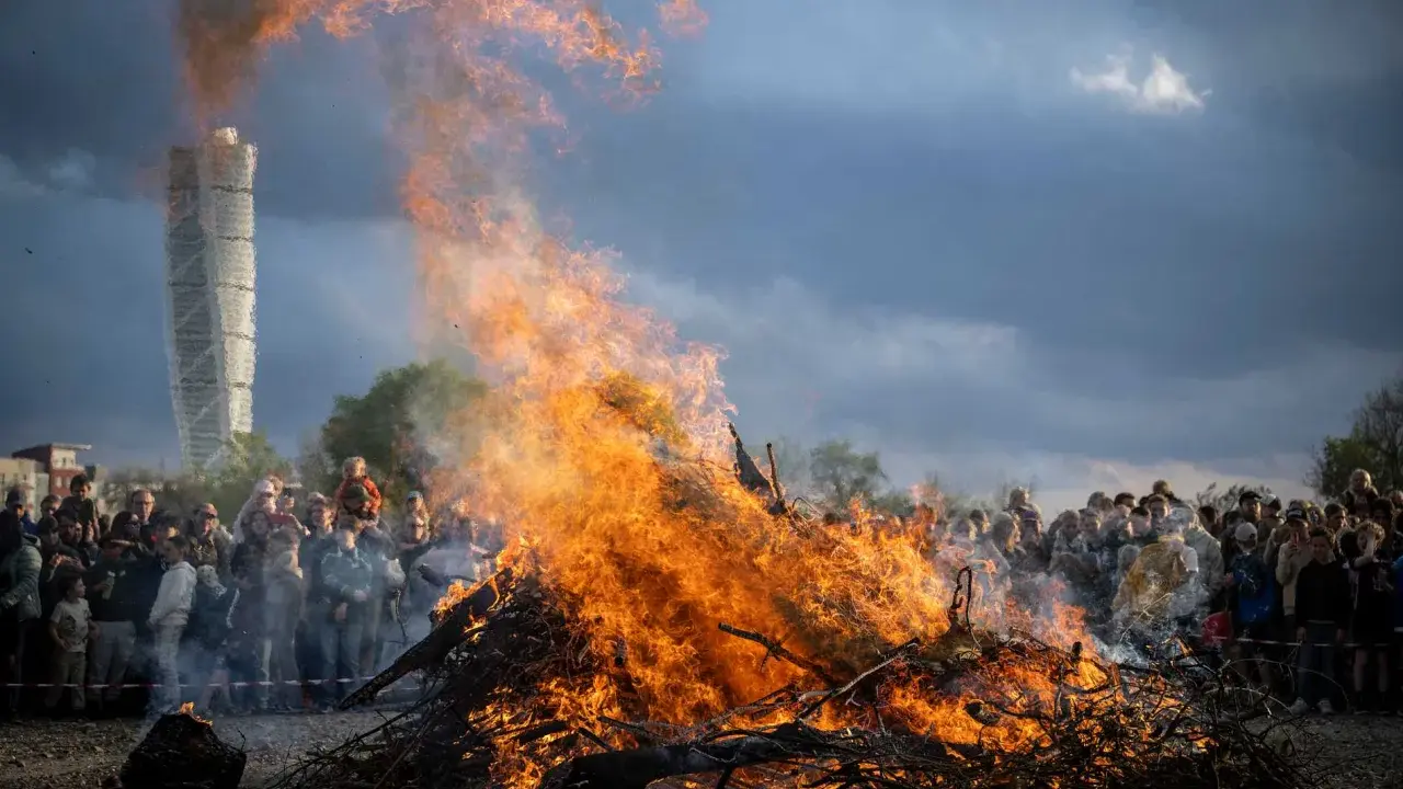 Stort bål med flammor som slår upp mot en dramatisk himmel. En folkmassa samlas för att bevittna ett traditionellt valborg firande.