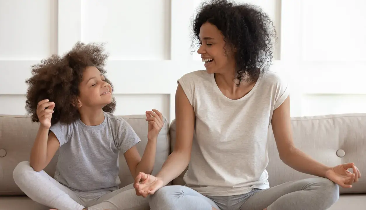 Madre e hija meditando juntas, fomentando sus habilidades de afrontamiento. Ambas sonríen y parecen relajadas.