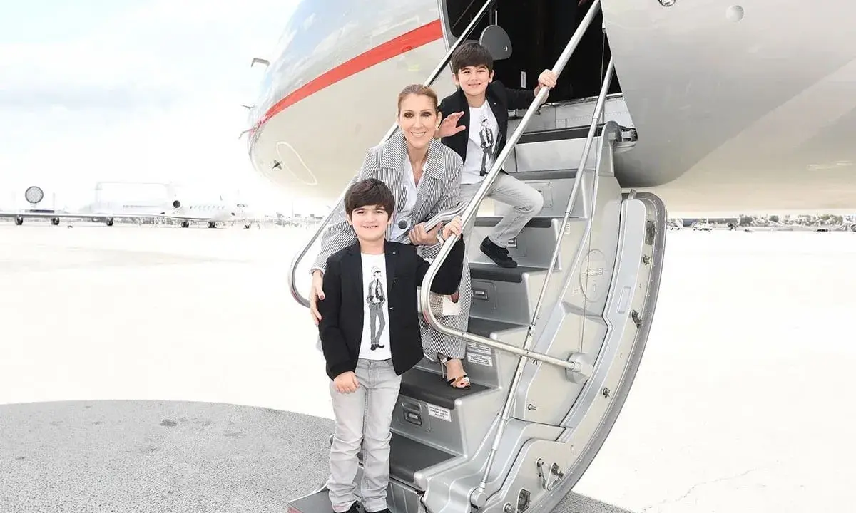Celine Dion med sina barn på trappan till ett privatjet. Familjen ser ut att vara på väg på en resa.