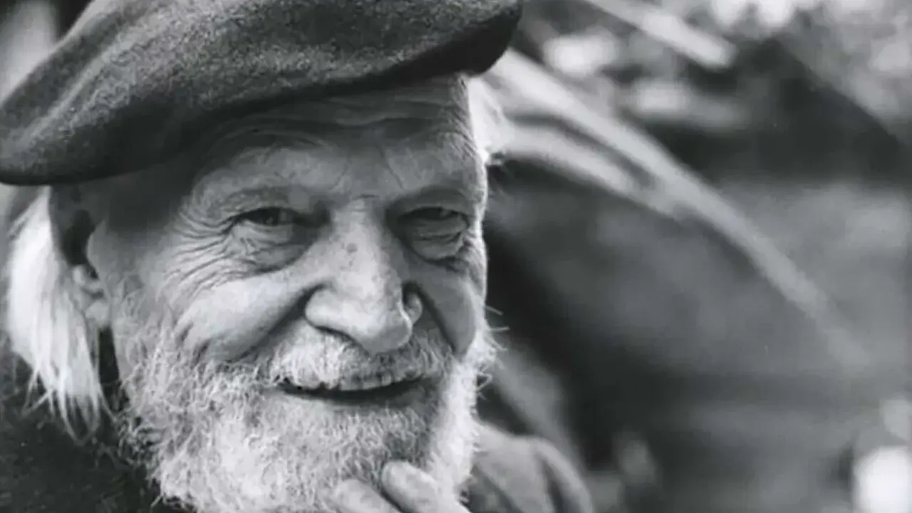 Un anziano con barba e berretto, il suo sorriso saggio evoca il significato che la morte si sconta vivendo appieno ogni istante.