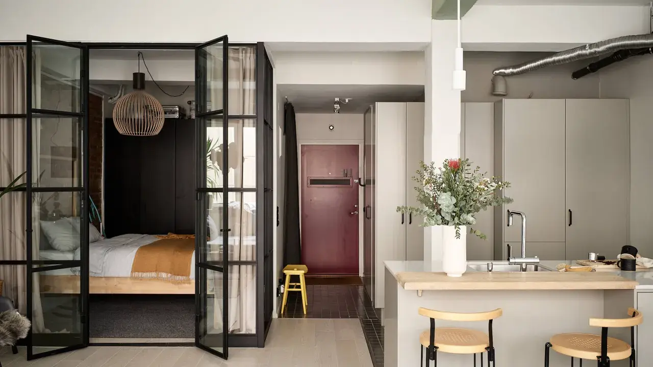 Une chambre en second jour, séparée par des portes vitrées. Une cuisine moderne avec un îlot et des tabourets complète l'espace.