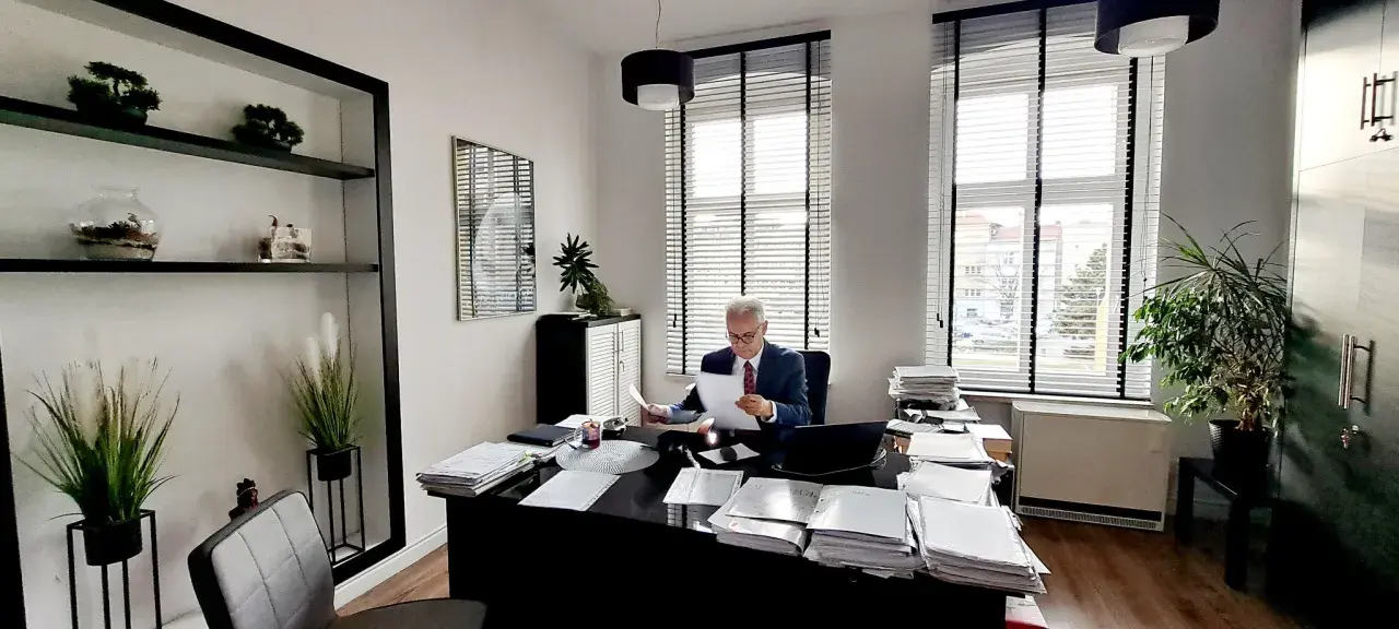 Adwokat w garniturze siedzi przy biurku w gabinecie, przeglądając dokumenty.