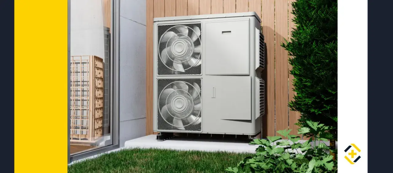 Unidad exterior de una bomba de calor para calefacción, instalada junto a una pared de madera y rodeada de vegetación.