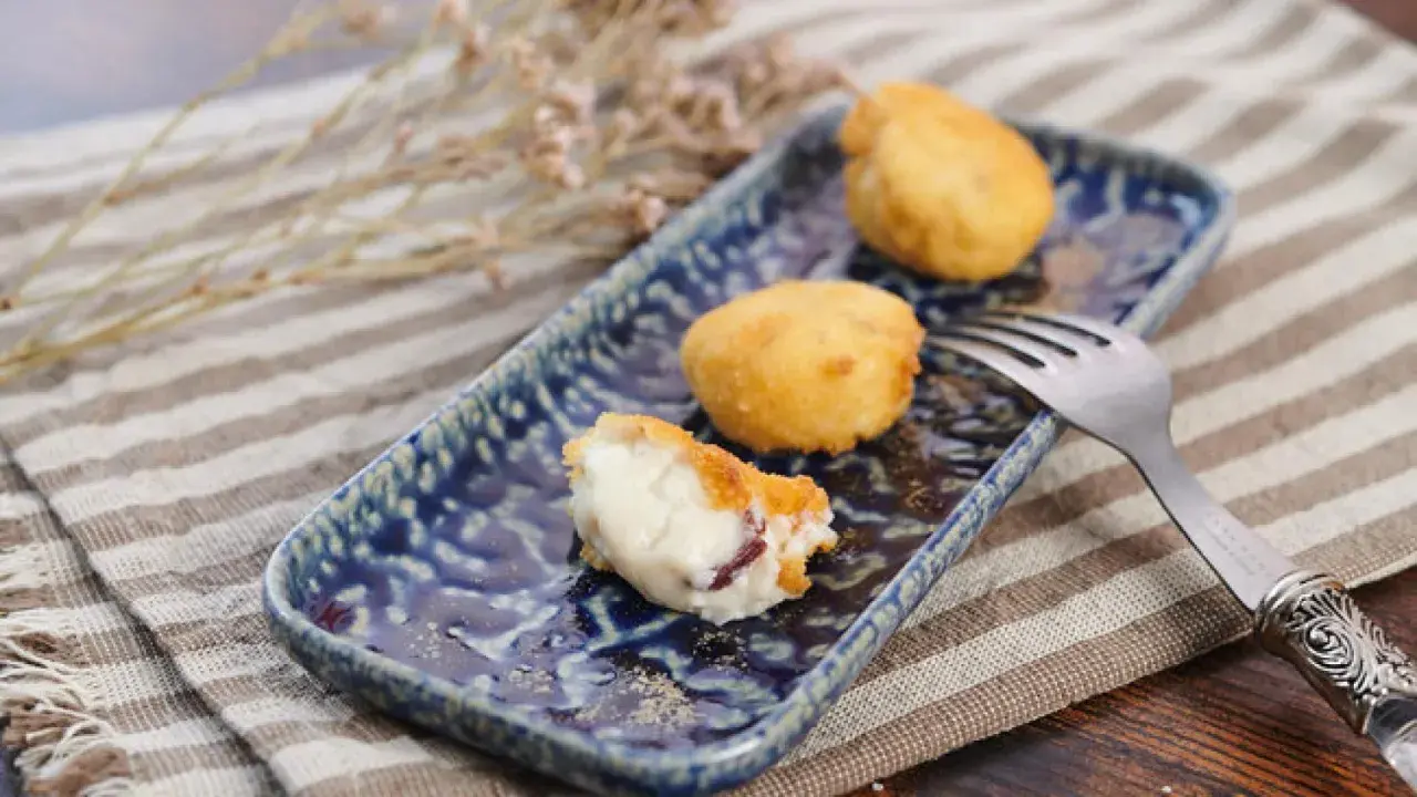 Deliciosa croqueta de jamón, cremosa por dentro y dorada por fuera, servida en un plato azul.