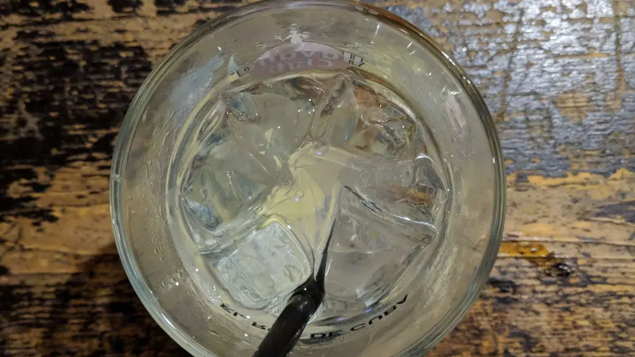 Ein Glas mit Eiswürfeln und einem schwarzen Strohhalm, bereit für einen erfrischenden Gin Tonic auf rustikalem Holztisch.