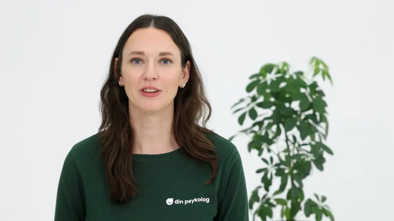 En kvinna med mörkt hår och blå ögon, klädd i en grön tröja med texten "din psykolog", talar. Bredvid henne står en grön växt. Hon ger dig verktyg att hantera sorg.