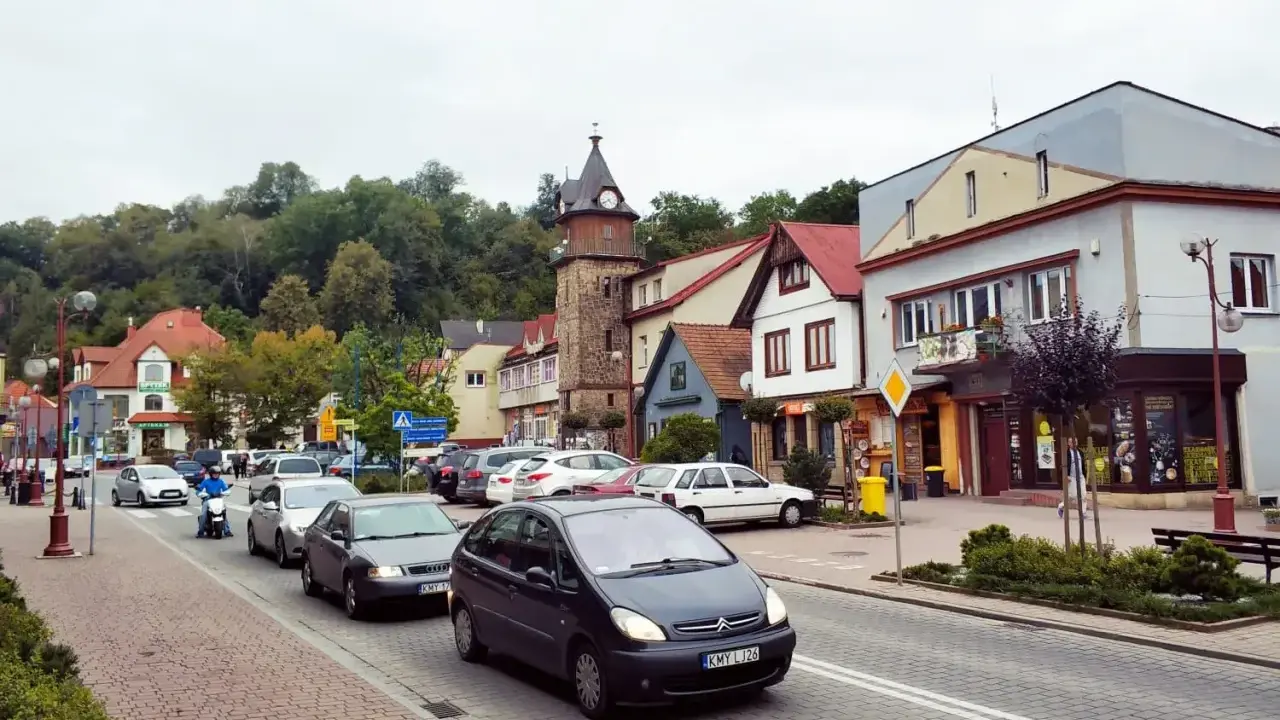 Tłoczny dobczyce rynek z wieżą zegarową, samochodami i skuterem.