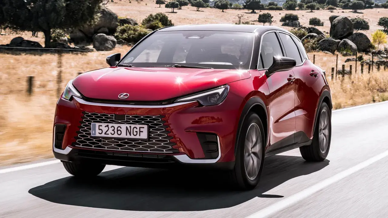 El Lexus LBX rojo brillante se desplaza por una carretera rural, con un paisaje seco y rocoso de fondo.