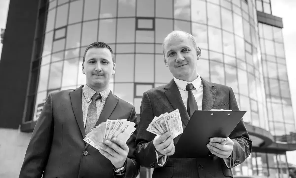 Dwóch mężczyzn w garniturach trzyma pieniądze i dokumenty. Ich aktywa rosną.