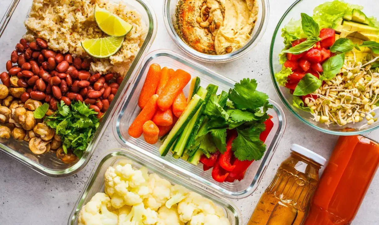 Gotowe pojemniki z jedzeniem na biwak bez gotowania: ryż z fasolą i pieczarkami, warzywa pokrojone w słupki, kalafior, sałatka z pomidorami i awokado, hummus i napoje.