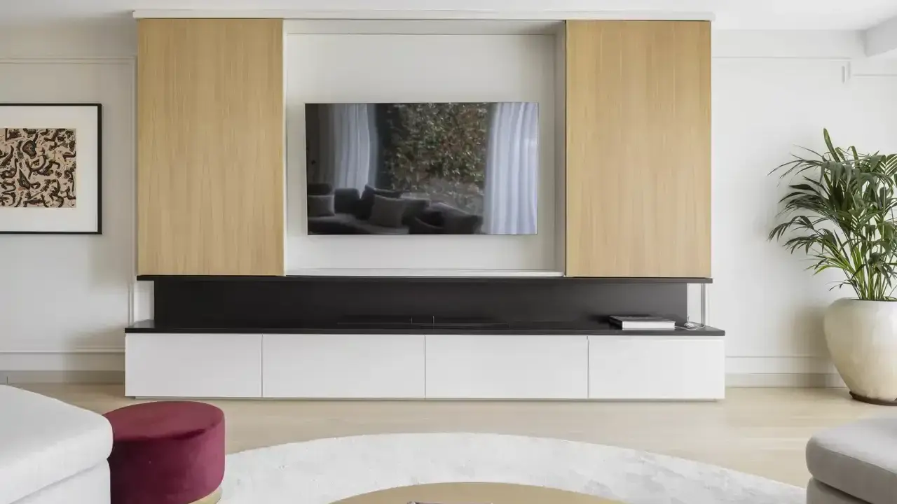 Un moderno mueble de salón con una gran televisión para poner la tele en medio del salón. Destacan los paneles de madera clara y los cajones blancos.