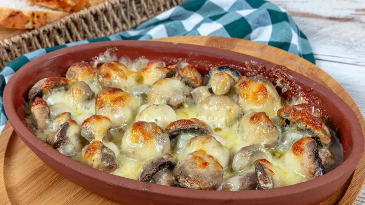Pieczarki zapiekane z serem w glinianym naczyniu, obok koszyk z pieczywem.