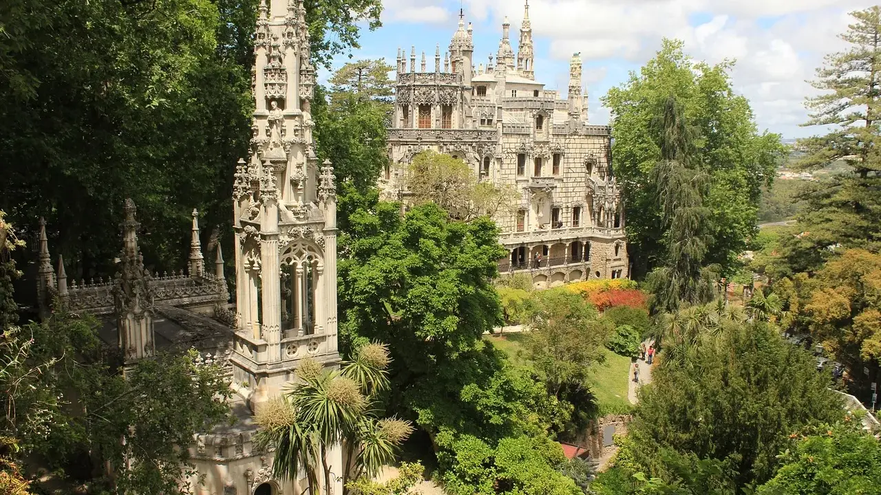 Sintra co zobaczyć: Quinta da Regaleira z wieżą i pałacem, otoczona bujną zielenią i kolorowymi rabatami.