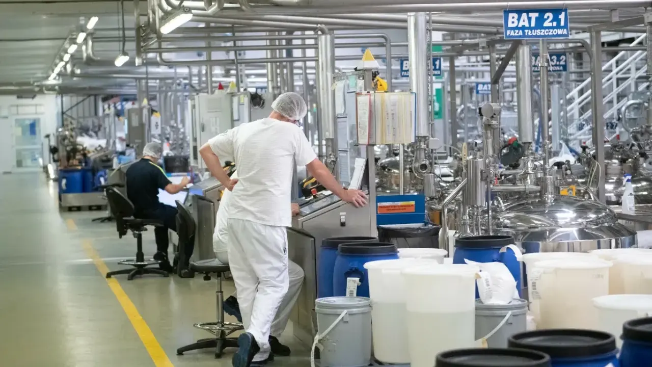Praca w Niemczech z zakwaterowaniem: pracownicy w białych kombinezonach nadzorują produkcję w nowoczesnej fabryce.
