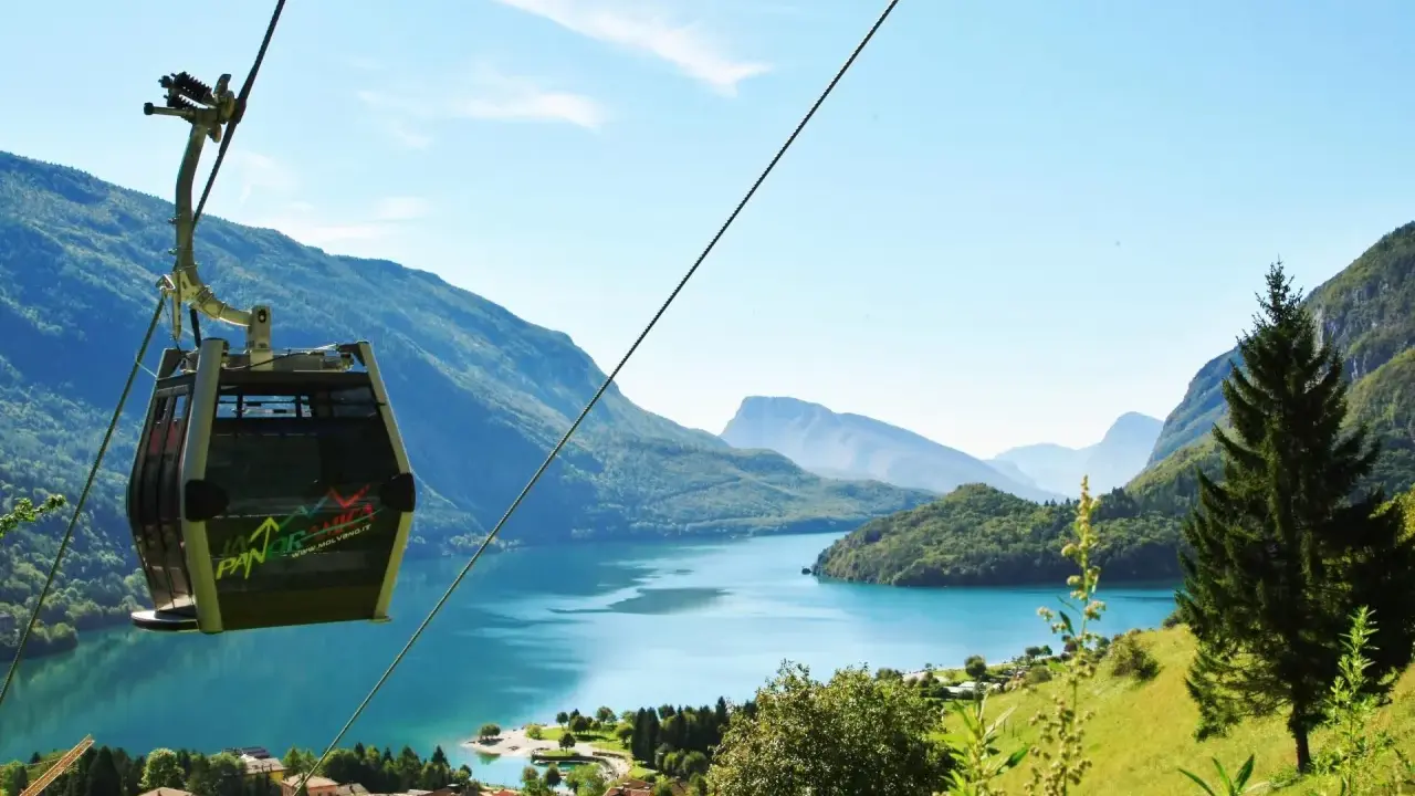 Cabina panoramica sul lago di Molveno, con montagne sullo sfondo. Si intravede una cascata tra gli alberi.