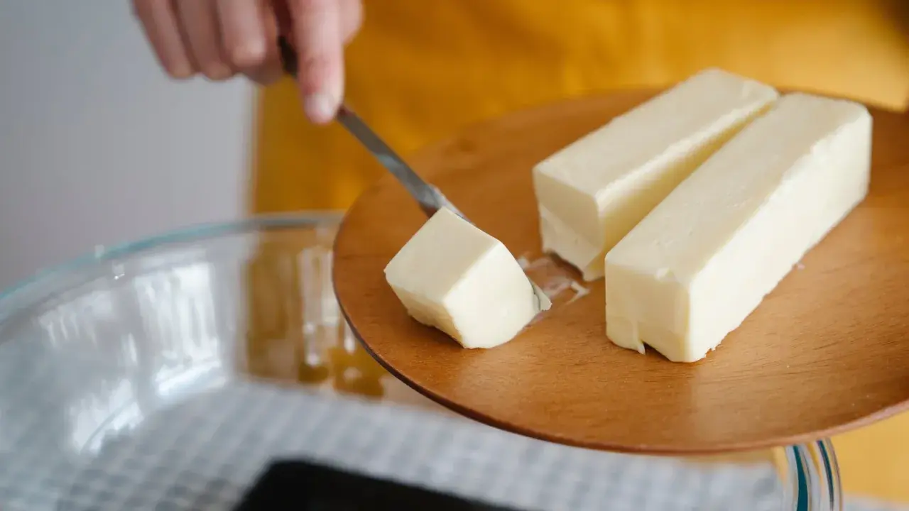Ein Stück Butter wird mit einem Messer von einem Holzbrett gehoben, bereit für die Zubereitung von Butterschmalz.