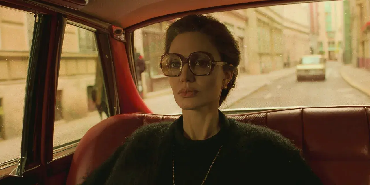 Angelina Jolie i en bil, en scen från en av hennes filmer. Hon bär stora glasögon och tittar ut genom fönstret.